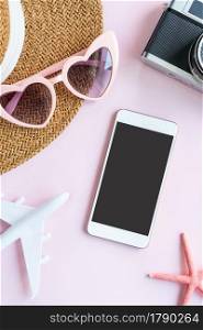 Flat lay of travel items and mobile phone on pink desk. Summer, holiday and planning travel concepts. Top view and copy space.