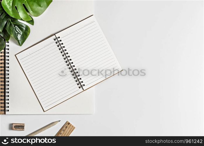 Flat lay of white office desk table with blank notebook, supplies and coffee cup. Top view with copy space.. blank sketchbook and green leaves