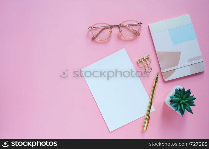 Flat lay of workspace desk, minimal stationery with note book, paper, pen, clip and eyeglasses on pink color background with copy space