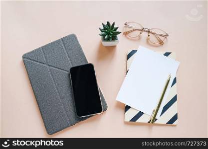 Flat lay of workspace desk, minimal stationery with smartphone and tablet, paper, pen, notebook and eyeglasses on yellow color background with copy space