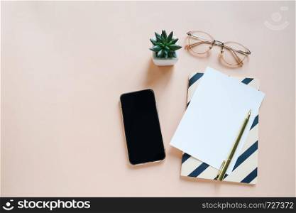 Flat lay of workspace desk, minimal stationery with smartphone, paper, pen, notebook and eyeglasses on yellow color background with copy space
