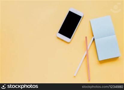 Flat lay of workspace desk with smartphone, note paper and pencil on bright yellow background, copy space and minimal style