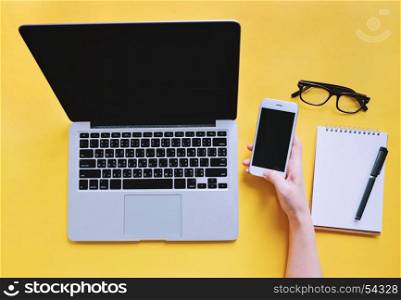Flat lay of workspace desk, woman hand using smartphone with laptop and blank notebook, business and technology concept