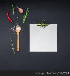 Flat lay overhead view blank recipe paper page with clip mockup text space invitation card on black background with greens herbs and spices. Menu recipe book food blog design with cooking ingredients