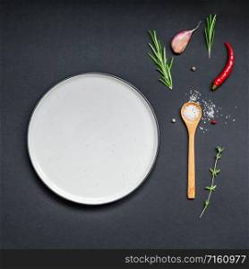 Flat lay overhead view empty plate mockup blank text space invitation card on black background with greens herbs and spices. Menu design food background with cooking ingredients