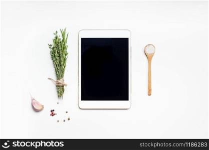 Flat lay overhead view tablet PC gadget mockup blank text space on white background with greens herbs and spices. Menu design food blog recipe cookbook or delivery app with cooking ingredients