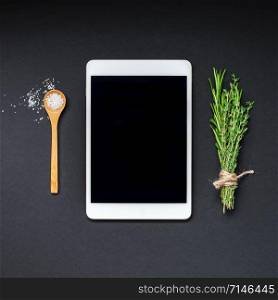 Flat lay overhead view tablet PC gadget mockup blank text space on black background with greens herbs and spices. Menu design food blog recipe cookbook or delivery app with cooking ingredients