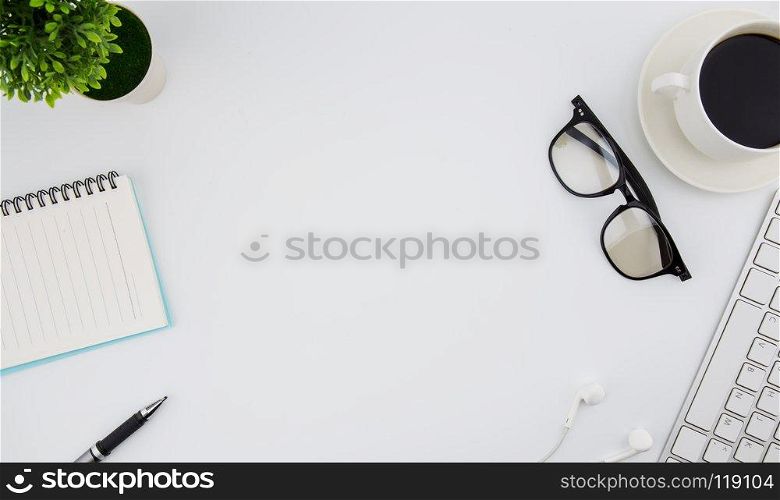 Flat lay photo of office desk with keyboard, notebook, earphone, glasses and coffee, top view