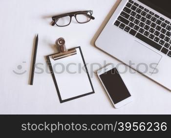 Flat lay photo of office desk with laptop, smartphone, eyeglasses and clipboard with copy space background&#xD;