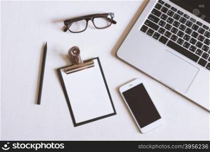 Flat lay photo of office desk with laptop, smartphone, eyeglasses and clipboard with copy space background&#xD;