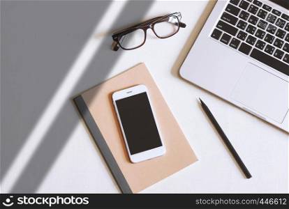 Flat lay photo of office desk with laptop, smartphone, eyeglasses and notebook with copy space background