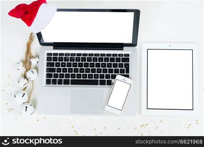 Flat lay scene of office table desk. Christmas workspace with laptop, tablet and phone and christmas deorations on white background, copy space on blank screen. Christmas mock up