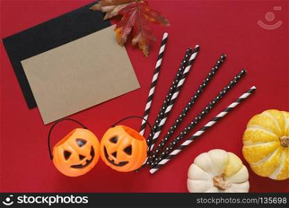 Flat lay style of halloween party concept with decorative pumpkins and black fancy straw with blank card on red background