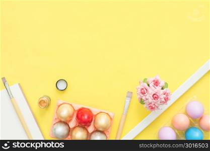Flat lay top view colorful easter egg painted in pastel colors composition and spring flowers with paint brush on yellow pastel color background. Easter day background top view with copy space.