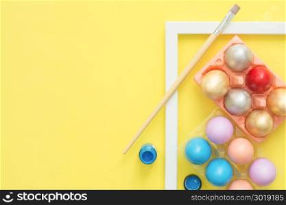 Flat lay top view colorful easter egg painted in pastel colors composition with paint brush on yellow pastel color background. Easter day background top view with copy space.