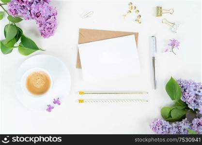 Flat lay top view home office workspace - blank card with lilac flowers on white background. Top view home office workspace