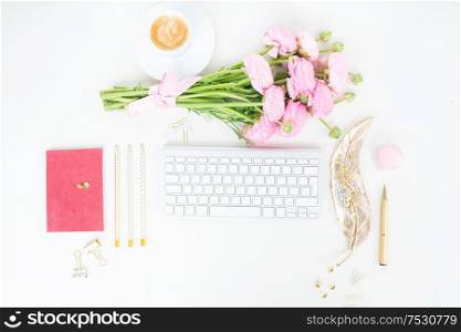 Flat lay top view home office workspace - modern keyboard with cup of coffee and pink ranunculus flowers. Top view home office workspace