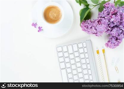 Flat lay top view home office workspace - modern keyboard with cup of coffee and lilac flowers on white background. Top view home office workspace