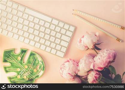 Flat lay top view home office workspace - modern keyboard with female accessories and peony flowers, copy space on pink background, toned. Top view home office workspace