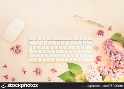 Flat lay top view home office workspace - modern keyboard with lilac flowers on pink background, toned. Top view home office workspace
