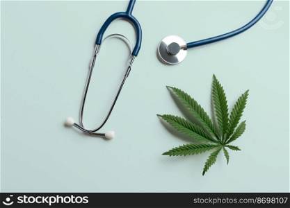 Flat lay top view image of a green sativa hemp leaf next to a stethoscope. Concept of legalized marijuana for medical purposes. Cannabis is being used in healthcare and medicine to treat illnesses.. Flat lay top view image of legalized green hemp leaf next to a stethoscope.
