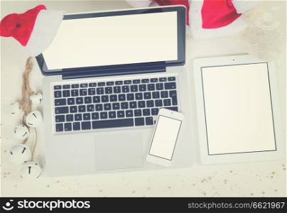 Flat lay, top view office table desk. Christmas workspace with laptop, tablet and phone and christmas deorations on white background, copy space on blank screen, retro toned. Christmas mock up