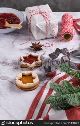 Flat lay with christmas cookies on marble surface with christmas decorative pine branch, jam, gift and cookie cutters.