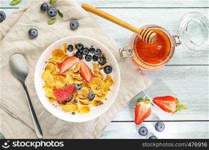 Flat lay with light healthy breakfast with corn flakes, berries and honey on white wooden table