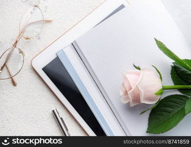 Flat lay women’s office desk. Female workspace with pink rose flower bouquet, dairy, glasses 