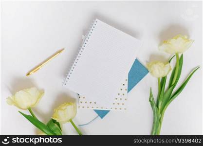 Flat lay workspace of a blogger or freelancer with yellow spring tulips, stationery on a white background with a blank sheet of notepad paper