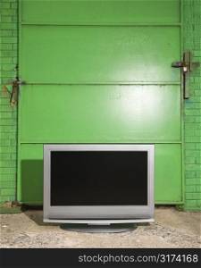 Flat panel television in front of green metal door.