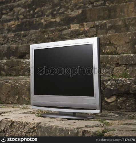 Flat panel television set in front of gray brick wall.