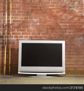 Flat panel television set in front of red brick wall.