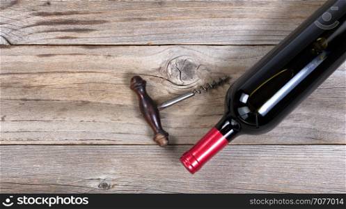 Flat view of a bottle of red wine with antique corkscrew opener on rustic wooden boards