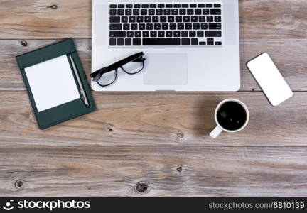 Flat view of working desktop consisting of laptop computer, coffee, cell phone, paper, pen and reading glasses.