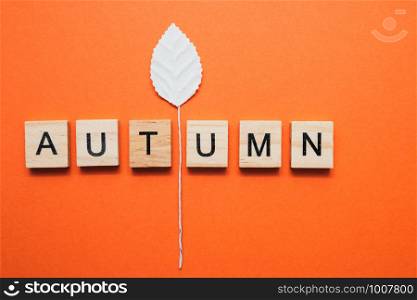 Flatlay from simple little white paper leaves and cube letters Autumn on orange background, autumn concept.. Flatlay from simple little white paper leaves and cube letters Autumn on orange background, autumn concept
