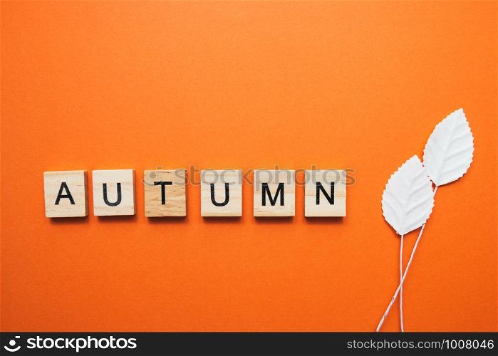 Flatlay from simple little white paper leaves and cube letters Autumn on orange background, autumn concept.. Flatlay from simple little white paper leaves and cube letters Autumn on orange background, autumn concept