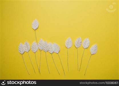 Flatlay from simple little white paper leaves on yellow background, autumn concept.. Flatlay from simple little white paper leaves on yellow background, autumn concept