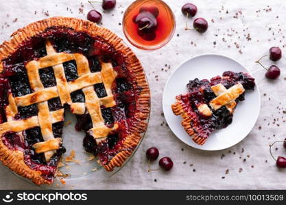 Flatlay still life of a baked cherry pie with a slice taken out and sitting on a plate near a cocktail.