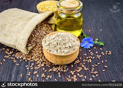 Flax flour in a bowl, seeds in a bag, blue linen flower and oil in a glass jar on a background of a dark wooden board