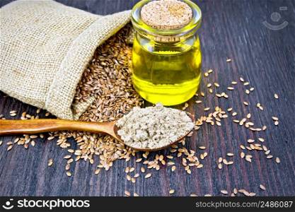 Flax flour in a spoon, oil in a glass jar, linen seeds in a bag on a dark wooden board background