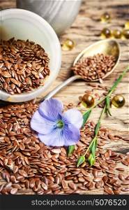 Flax seeds in spoons and bowl. Flax seed and flowering buds of flax on a wooden background
