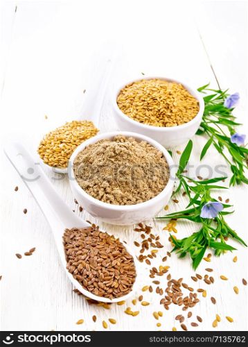 Flaxseed flour in a bowl, white and brown linen seeds in two spoons and on table, leaves and blue flax flowers on white wooden board background