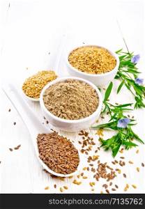 Flaxseed flour in a bowl, white and brown linen seeds in two spoons and on table, leaves and blue flax flowers on white wooden board background