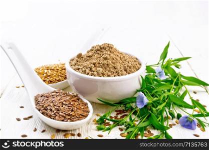 Flaxseed flour in a bowl, white and brown linen seeds in two spoons and on table, leaves and blue flowers of flax on light wooden board background