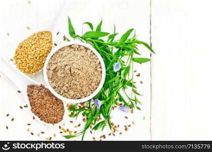 Flaxseed flour in a bowl, white and brown linen seeds in two spoons and on table, leaves and blue flax flowers on wooden board background from above