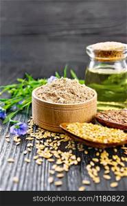 Flaxseed flour in a bowl, white and brown seeds in spoons and on table, flax leaves and flowers, oil in a glass jar on wooden board background