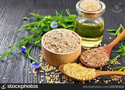 Flaxseed flour in a bowl, white and brown seeds in two spoons and on table, flax leaves and flowers, oil in a glass jar on dark wooden board background