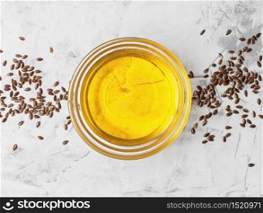 Flaxseed oil in a glass bowl and golden flax seeds on a gray background, top view. Useful natural oil.