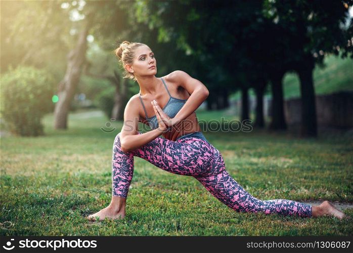 Flexible woman meditating, yoga training on the grass in summer park. Morning yogi meditation